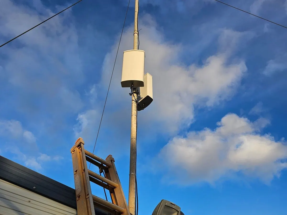 Two white panel antennas on a guyed mast above a site building